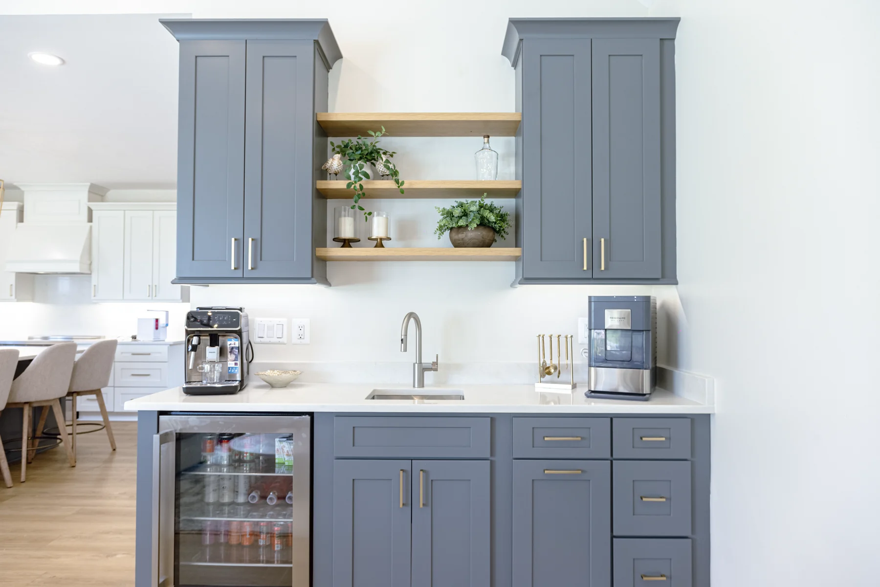 Kitchen beverage station with blue-gray cabinetry, brass hardware, and open wood shelving